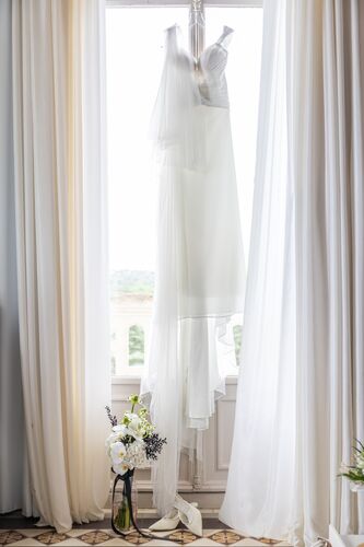 Robe de mariée suspendue devant une fenêtre du Château Valmy